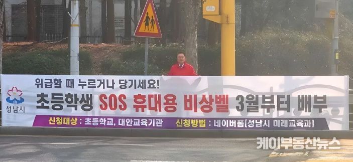 황금석 성남시의원이 초등학교 인근에 설치된 ‘초등학생 SOS 휴대용 비상벨’ 신청 안내 현수막 앞에 서 있다